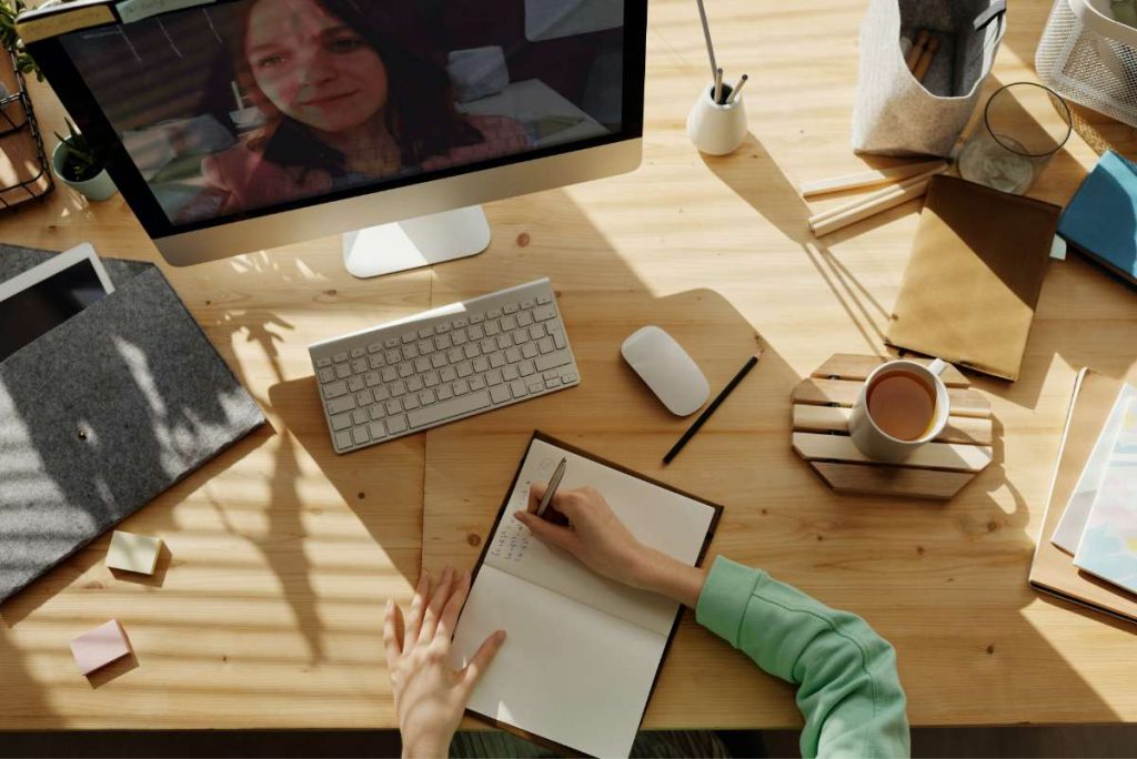 Videollamada de teletrabajo Escritorio con ordenador en videollamada y chica tomando apuntes