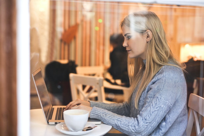 Mujer sentada en café anotando en macbook Los 4 pasos de oro que te ayudarán a elaborar un plan de marketing digital, paso nro 1