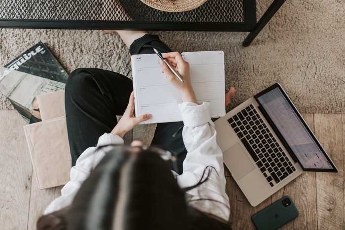 Mujer sentada con libreta y macbook Los 4 pasos de oro que te ayudarán a elaborar un plan de marketing digital