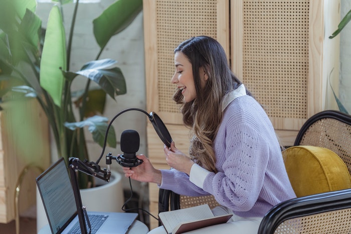 Chica con micrófono creando podcast Podcast: Qué es y cómo puedes crear uno para tu marca, Pasos que debes seguir para crear, editar y subir un podcast